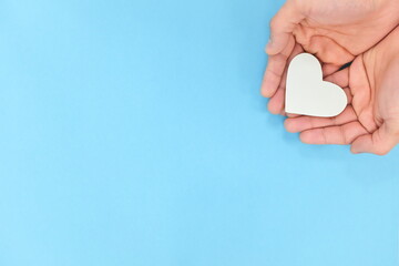 Cupped hands holding a white heart in blue background. Charity, pure love, compassion and kindness concept. Top view.