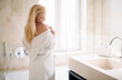 © JustLife - Beautiful woman enjoying in hotel. Young happy woman in bathrobe use the cream for the body.