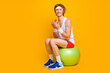 Portrait of his he nice attractive funky cheerful cheery sportive guy sitting on fitball eating forbidden tasty yummy food isolated over bright vivid shine vibrant yellow color background