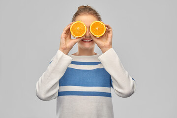 Wall Mural - healthy eating, fun and people concept - funny smiling teenage girl in pullover with orange halves instead of eyes over grey background