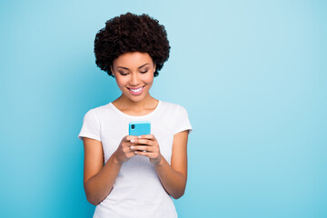 Canvas Print - Photo of cheerful beautiful dark skin curly lady holding telephone hands chatting friends sending new pictures wear casual white t-shirt isolated blue color background