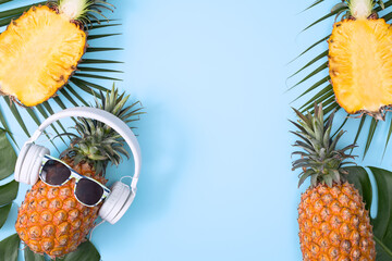 Wall Mural - Funny pineapple wearing white headphone, concept of listening music, isolated on colored background with tropical palm leaves, top view, flat lay design.