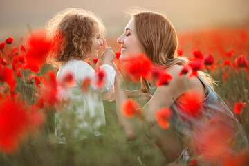 Beautiful smiling child girl with mother are having fun in field of red poppy flowers over sunset lights