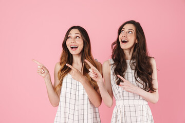 Wall Mural - Image of excited caucasian women smiling and pointing fingers aside