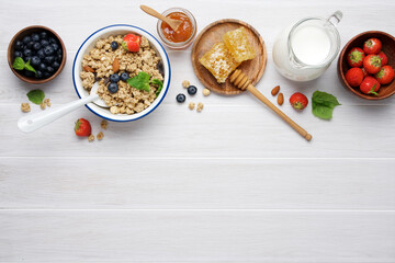 Wall Mural - Granola with berries, milk and honeycombs. Bright healthy breakfast on white wooden background