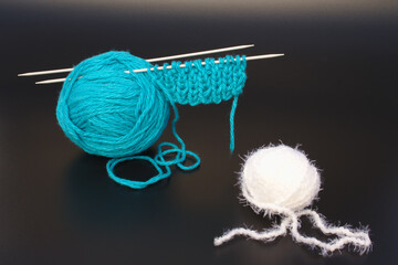 Knitting threads in blue and white and knitting needles on a black background.