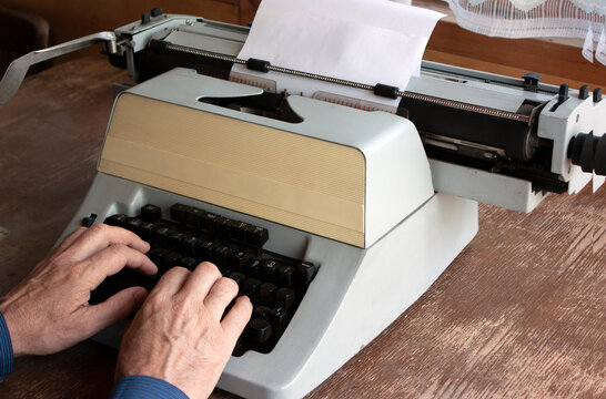 Vintage typewriter stands on an old wooden table, the writer prints text on paper