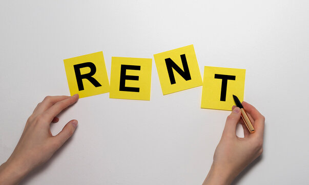 The word RENT printed on yellow clipped stickers notes on white wall with female hands. Renting concept