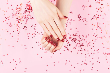 Manicure and nailcare concept. Two woman hands and falling confetti on pink background. Flat-lay, top view. Copy space.