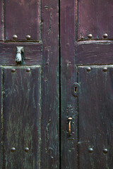 Old rustic wooden door with different layers of cracked paint  and hand knocker