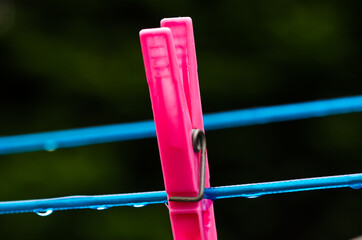 Wall Mural - A blue clothing line with many raindrops at the string in front of a dark background, with a pink peg after the rain. Retro way of doing the laundry.