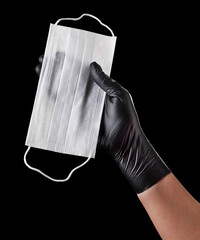 Wall Mural - Hand in black gloves holding disposable face mask isolated on black background