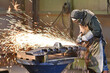 © industrieblick - Workers in protective equipment in a foundry work on a casting with a grinding machine at the workplace