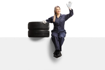 Sticker - Female auto mechanic worker in a uniform sitting on a panel with tires and waving