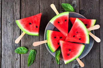 Wall Mural - Watermelon slice popsicles on a dark serving plate, top view against a rustic wood background