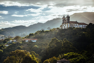 Wall Mural - Landscape of Ouro Preto city of Minas Gerais, Brazil with Sao Francisco de Paula Church at foreground with sunlight and clouds rounded by green florest and trees 