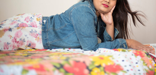 Wall Mural - half face portrait of Indian Bengali beautiful and cute brunette girl in a casual blue jeans shirt is reading newspaper lying on bed in relaxing and casual mood. Indian lifestyle and fashion portrait