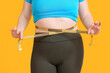 © Pixel-Shot - Woman with excess weight measuring her waist on color background