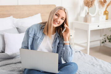 Canvas Print - Beautiful young woman with laptop talking by mobile phone at home