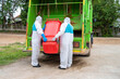 © visoot - Stop biohazard,Garbage men in coronavirus hazmats working together on emptying dustbins for trash removal with truck loading waste and trash bin.