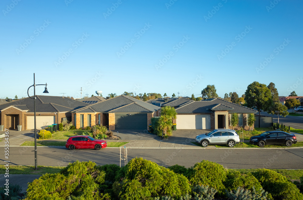 Elevated view of modern suburban homes in an Australian suburb with family cars parked on side of the street. - obrazy, fototapety, plakaty 