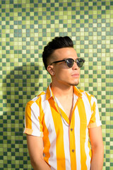 Young handsome multi ethnic man with sunglasses thinking against green background