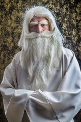 Wall Mural - A grey-haired bearded severe wizard in a white cloak is doing magic against dark-gold background.