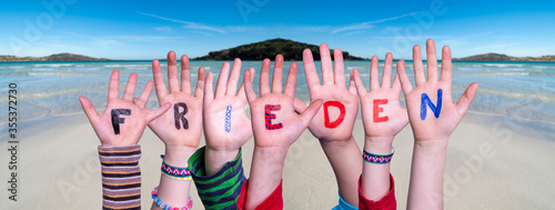 Children Hands Building Colorful German Word Frieden Means Peace. Ocean And Beach As Background