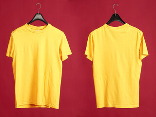 Exclusive hanger with empty yellow t-shirt hanging isolated on a red background. Blank yellow male tshirt template, from two sides,  for your mockup design to be printed.