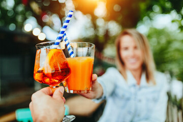 Celebrating life. Toast with aperol spritz. Young smiling woman in background.