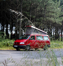 Red Van With Roof Up. Campervan Parked Next To Forest.