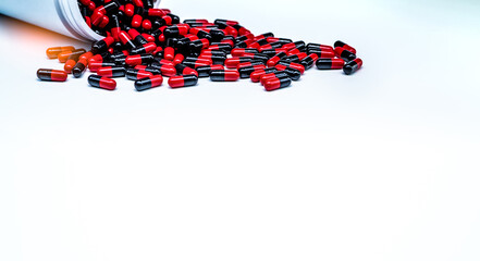 Wall Mural - Red-black antibiotic capsule pills spread out of plastic drug bottle on white background. Antibiotic drug resistance. Pharmaceutical industry. Pharmaceutical manufacturing. Capsule pills production.