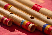Close Up Of Different Sizes Hindu Bamboo Flute Called Bansuri On A Red Table.