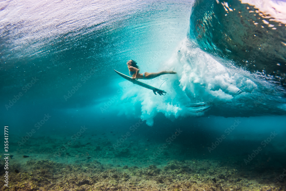 woman in bikini doing duck dive with the surfboard under the waves - obrazy, fototapety, plakaty 