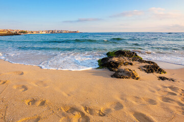 sandy beach with rocks. sunny morning in the resort town. wave brings seaweed on the stones on the shore. beautiful summer vacation landscape with clouds on the blue sky