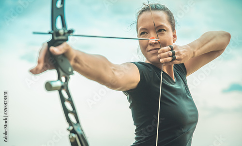 Fotomural archery, young woman with an arrow in a bow focused on hitting a target