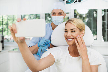 Beautiful and happy blonde woman at beauty medical clinic. She is sitting and talking with female doctor about face esthetics treatment.