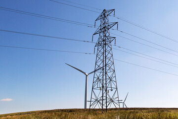 Electricty pylon with power lines erected in front of a wind turbine with a blue sky background. Renewable energy concept.