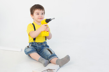 Wall Mural - a small boy in a Builder's suit makes repairs on a white background