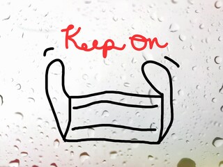 Keep on with face mask drawing on glass window with raindrops outside