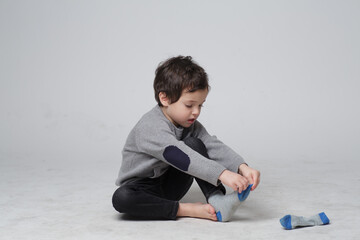 Portrait of Cute little kid sitting learning how to put the socks on by him self, Happy Toddler boy pulling his socks to his foot, Child development, skills concept.