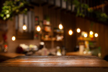 Empty Wooden Table Top On Blur Light Golden Bokeh Of Cafe Restaurant, Bar In A Dark Background.