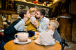 © sofiko14 - Happy lovely family, young pleasant parents and their two little sons, enjoying time together, sitting in cafe and having tasty lunch dinner with croissants. Mom and dad kissing their little son