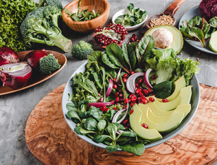 Healthy fresh salad with avocado, greens, arugula, spinach, pomegranate in plate over grey background. Healthy vegan food, clean eating, dieting, top view