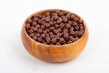 Wooden bowl with chocolate corn balls and spoon on white background