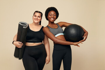 Workout. Diversity Women Portrait. Multi-Ethnic Slim And Plus Size Models Against Beige Background. African And Caucasian Women In Black Sportswear Holding Pilates Ball And Mat. Fitness As Lifestyle.