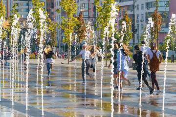 Photography of teenagers running through the fountains set. Concepts of walking, happiness, childhood and freshness in hot summer day. 