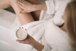 © JustLife - Close up of woman in bathrobe use the cream for the body.