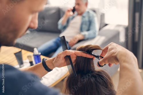 Fotografía Concentrated man cutting hair with scissors and comb