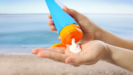 Young woman applying sun protection cream near sea, closeup